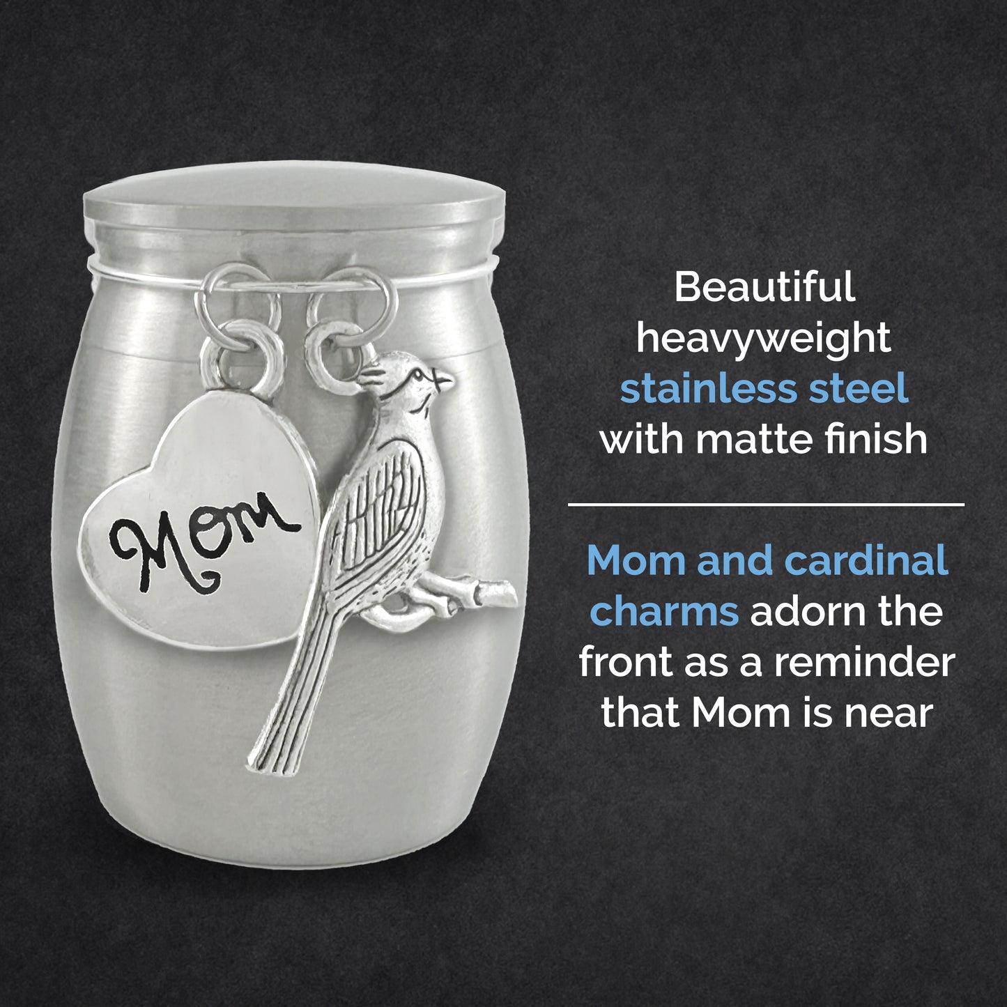 A silver-toned metal jar-shaped keepsake urn with a matte finish, featuring a hanging heart charm engraved with 'Mom' and a cardinal bird charm. The product is shown against a dark textured background with descriptive text on the right. The descriptive text reads: beautiful heavyweight stainless steel with matte finish. Mom and cardinal charms adorn the front as a reminder that mom is near.