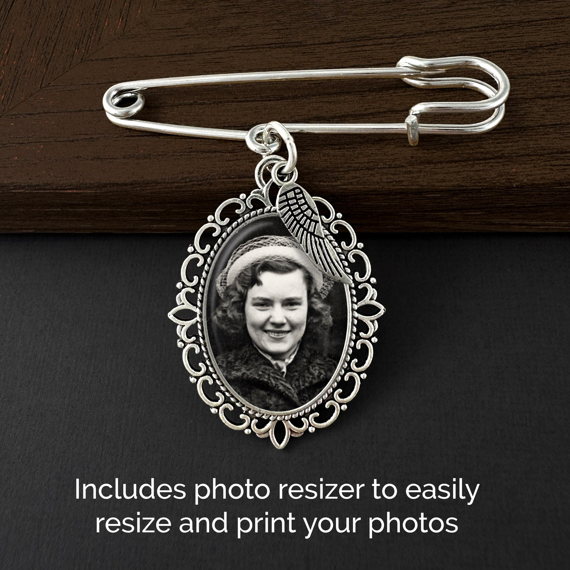 A silver wedding bouquet photo charm pin with an ornate oval frame and a guardian angel wing shown on a dark wood and black background. The frame contains a sample black-and-white portrait photo, and text at the bottom reads, 'Includes photo resizer to easily resize and print your photos.'