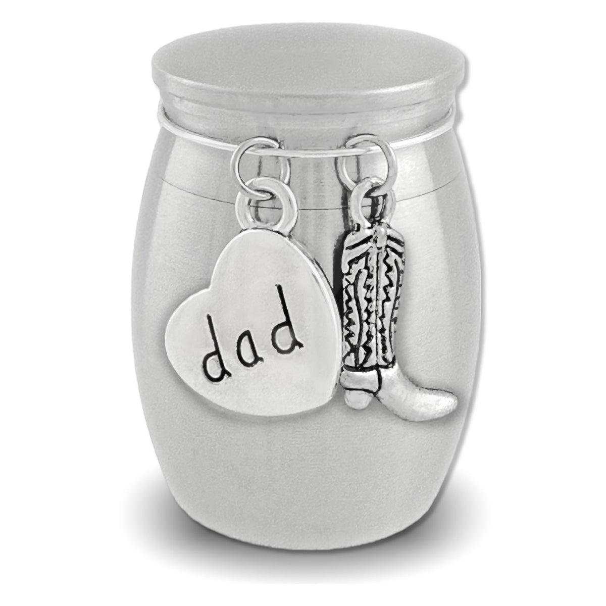 A silver cremation urn shaped like a small jar with a lid, featuring dangling charms: a heart-shaped charm engraved with 'dad' and a cowboy boot charm, shown on a white background.