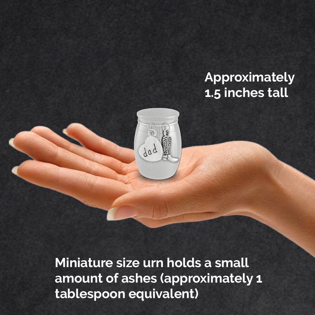 A hand holding a miniature silver cremation urn with a heart-shaped tag that says 'dad' and a small cowboy boot charm. White text on a dark background explains the product size, noting it is approximately 1.5" tall.