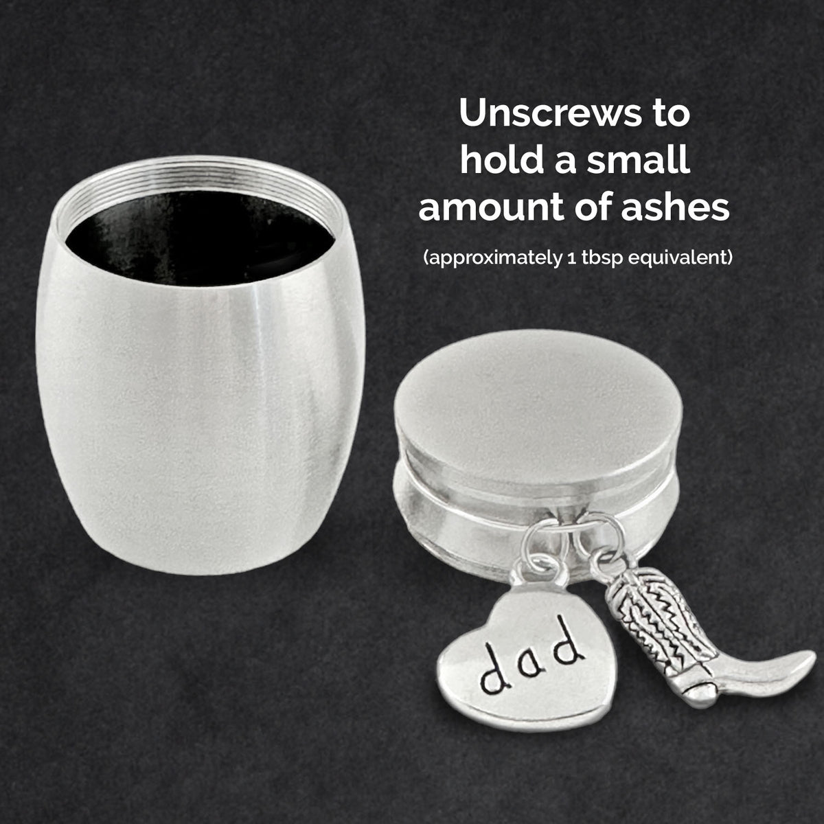 A silver metal cremation ashes holder  shown open on a dark background, with the main container open on the left and a the lid with cowboy boot charm and heart tag engraved 'dad' on the right. White text reads 'Unscrews to hold a small amount of ashes (approximately 1 tbsp equivalent)'.