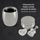 A brushed silver small stainless steel urn shown open on a dark textured background, with the open round container on the left and the round lid on the right. A heart-shaped charm engraved with 'dad' and a guitar-shaped charm hang from the top.