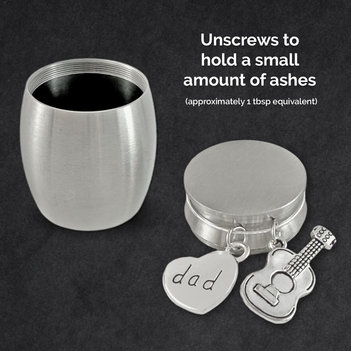 A brushed silver small stainless steel urn shown open on a dark textured background, with the open round container on the left and the round lid on the right. A heart-shaped charm engraved with 'dad' and a guitar-shaped charm hang from the top.
