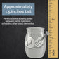 A small stainless steel urn with two silver charms, one heart-shaped and one guitar-shaped, displayed on a dark textured background with a wooden ruler on the right and text stating it is approximately 1.5 inches tall.