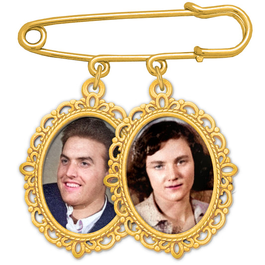 A gold safety pin brooch with two dangling oval photo frames, shown on a plain white background. The left frame contains a portrait of a smiling young man, and the right frame contains a portrait of a young woman.