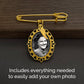 Gold wedding bouquet photo charm pin with angel wing charm and ornate oval frame, shown on a dark wood and black background with text reading 'Includes everything needed to easily add your own photo'.