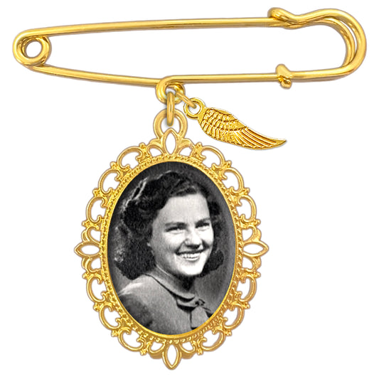 Gold wedding bouquet photo charm pin with angel wing charm and ornate oval frame holding a black-and-white portrait photo of a woman shown on a plain white background.