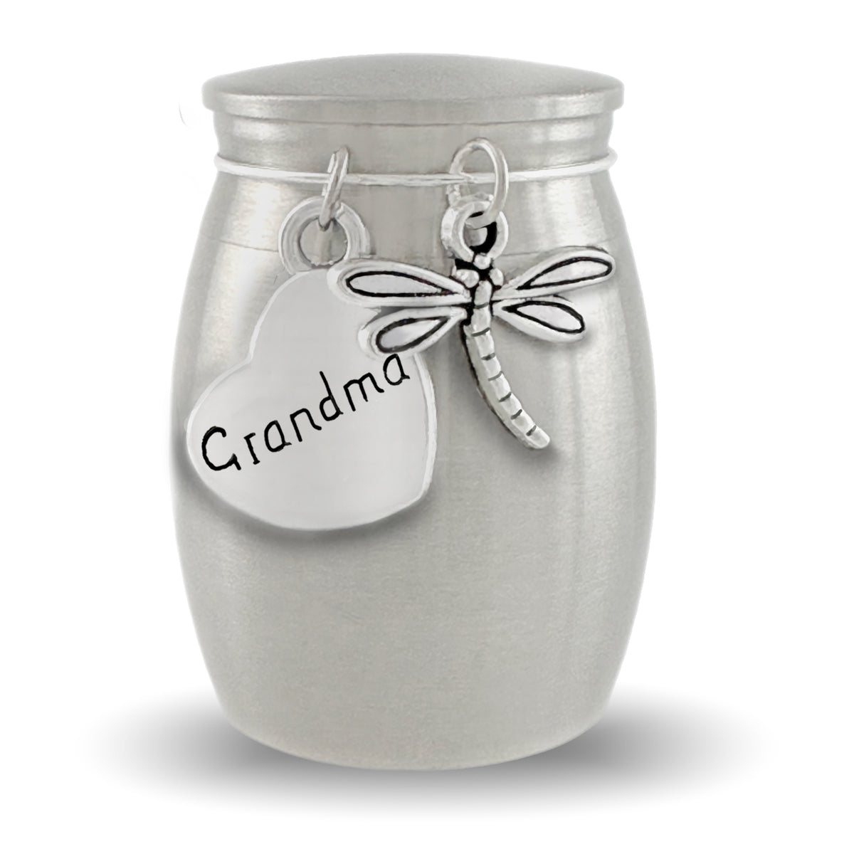 A silver cremation urn shaped like a small jar with a lid, featuring a heart-shaped tag engraved with 'Grandma' and a dragonfly charm, shown on a white background.