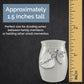 A small silver urn, decorated with a silver dragonfly charm and a heart tag that says 'Grandma', shown on a dark textured background with a yellow inch ruler and text stating it is approximately 1.5 inches tall.