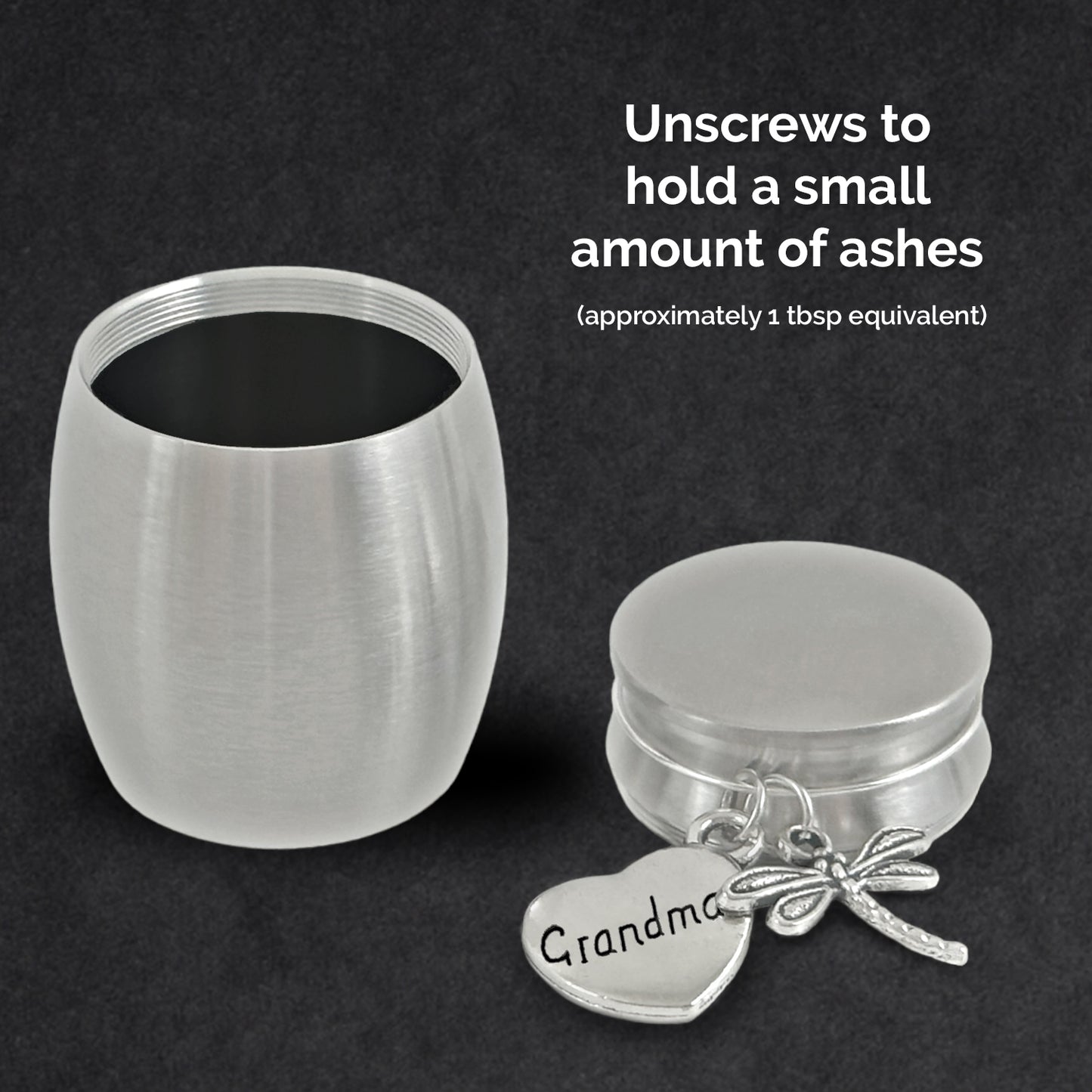 A brushed silver metal miniature size cremation urn with a heart-shaped charm engraved 'Grandma' and a dragonfly charm, shown with the lid unscrewed on a dark textured background with instructional text.