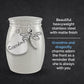 A silver-toned metal little urn with engraved 'Grandma' text on a heart-shaped charm and a dragonfly charm, shown on a dark textured background with descriptive text on the right.