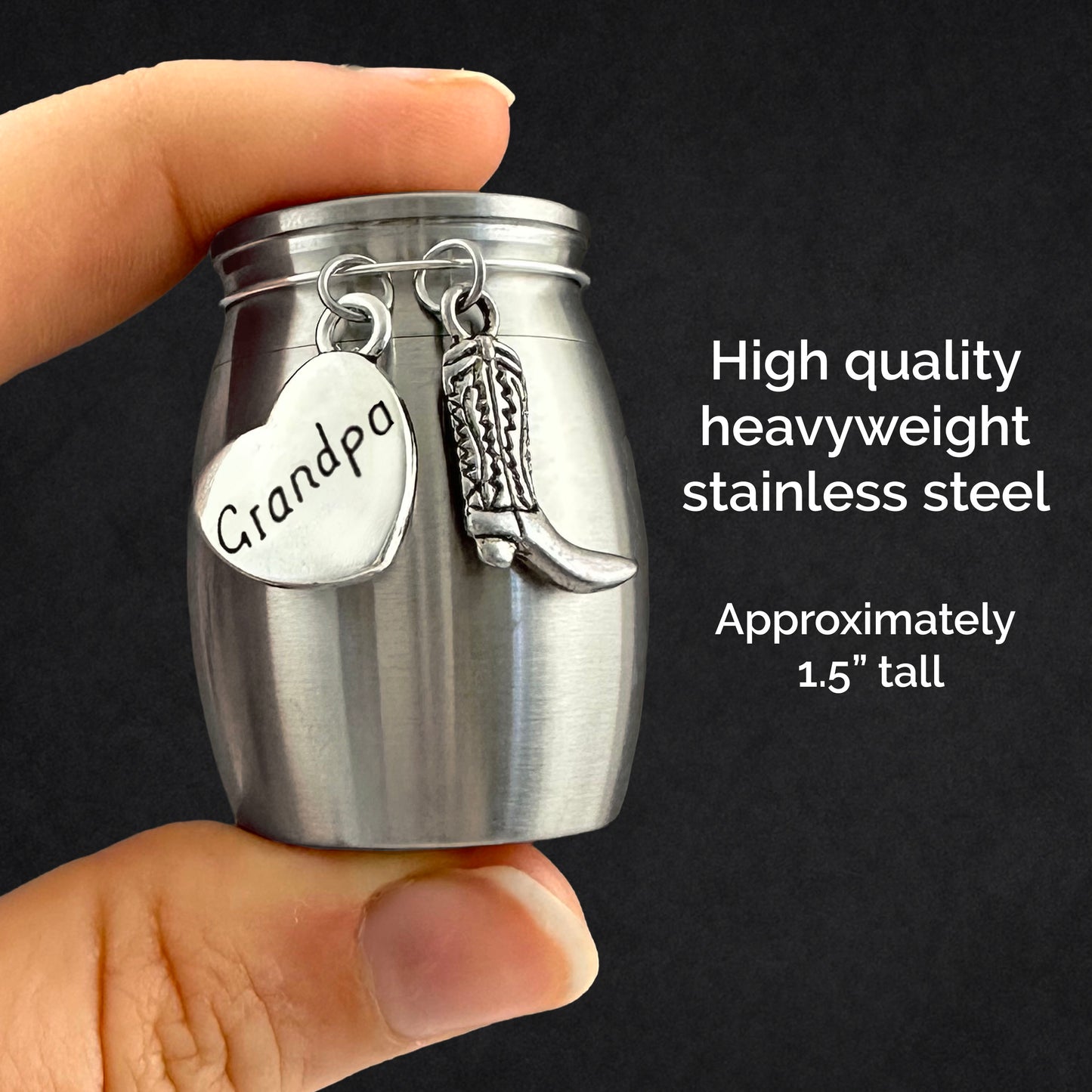 A hand holds a small stainless steel memorial jar with a heart-shaped charm engraved 'Grandpa' and a cowboy boot charm, against a dark background with text describing the product.