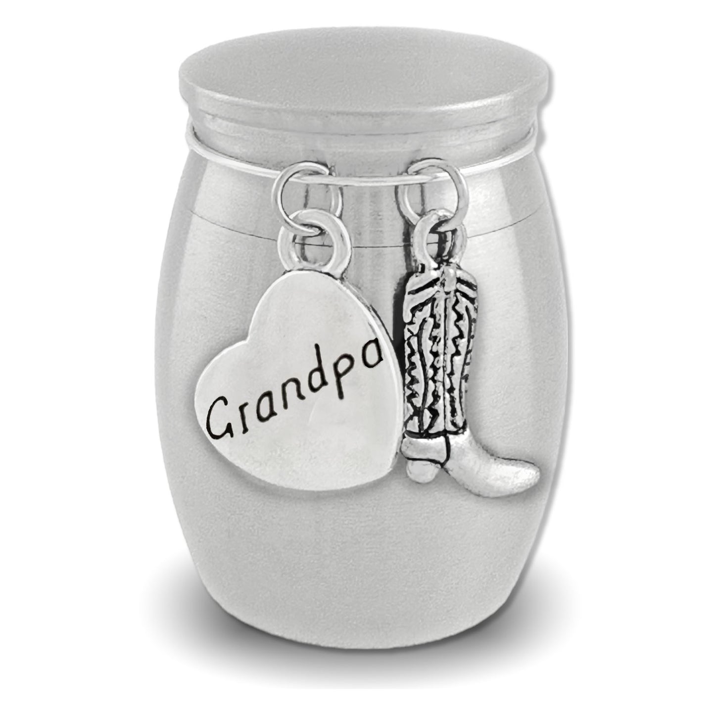 A silver cremation urn shaped like a small jar with a lid, featuring dangling charms: a heart-shaped charm engraved with 'dad' and a cowboy boot charm, shown on a white background.