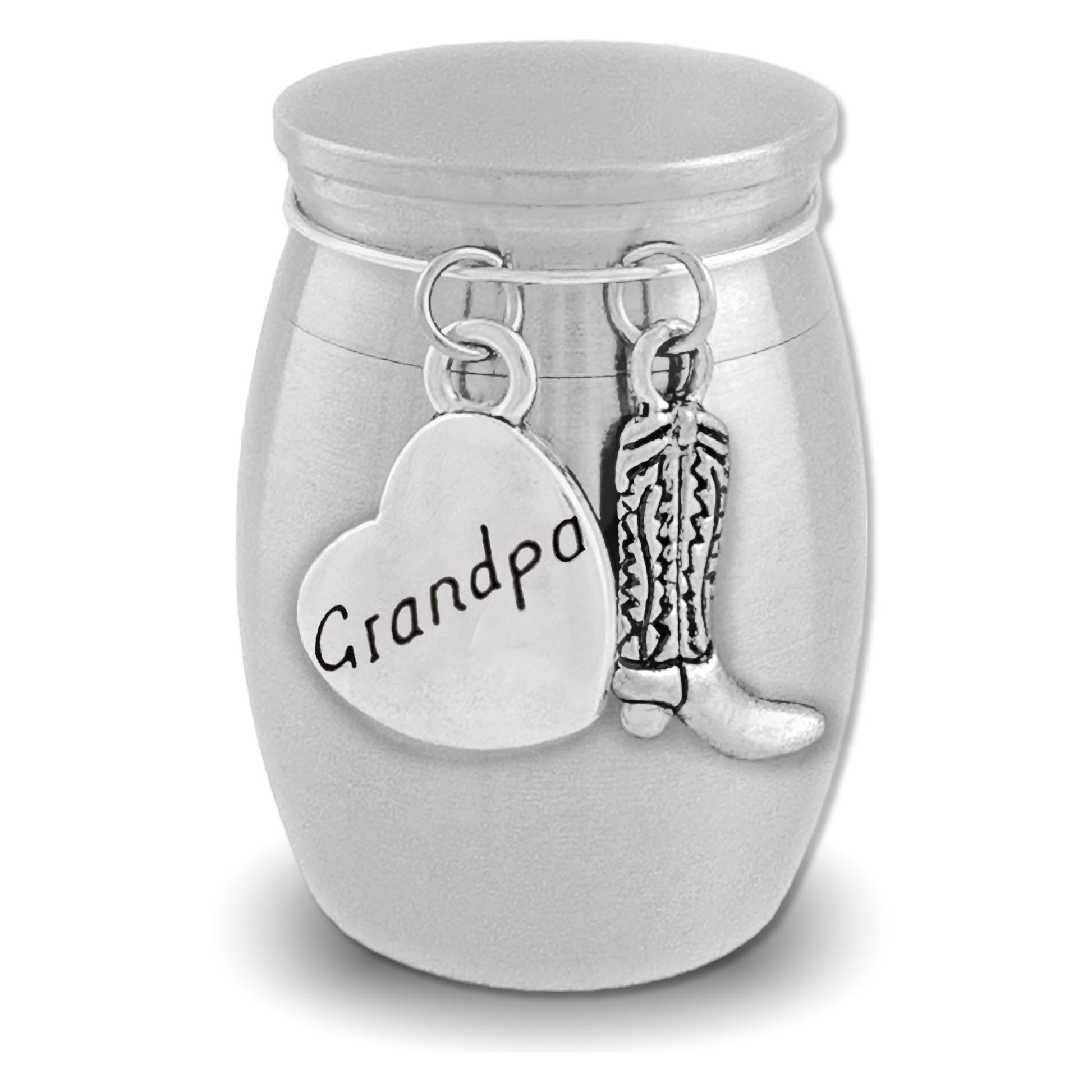 A silver cremation urn shaped like a small jar with a lid, featuring dangling charms: a heart-shaped charm engraved with 'dad' and a cowboy boot charm, shown on a white background.