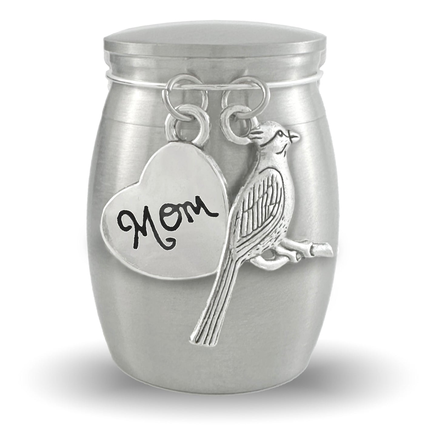 A silver cremation urn shaped like a small jar, featuring a heart-shaped charm engraved with 'Mom' and a cardinal charm, shown on a white background.