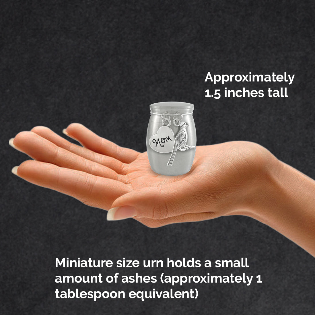 A hand holding a miniature silver urn with the charm reading 'Mom' and a cardinal bird charm, set against a dark textured background with text explaining its size and ash capacity.