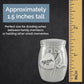 A brushed silver keepsake urn featuring a heart-shaped tag engraved 'Mom' and a cardinal bird charm, shown on a dark textured background with a yellow inch ruler and text stating it is approximately 1.5 inches tall.