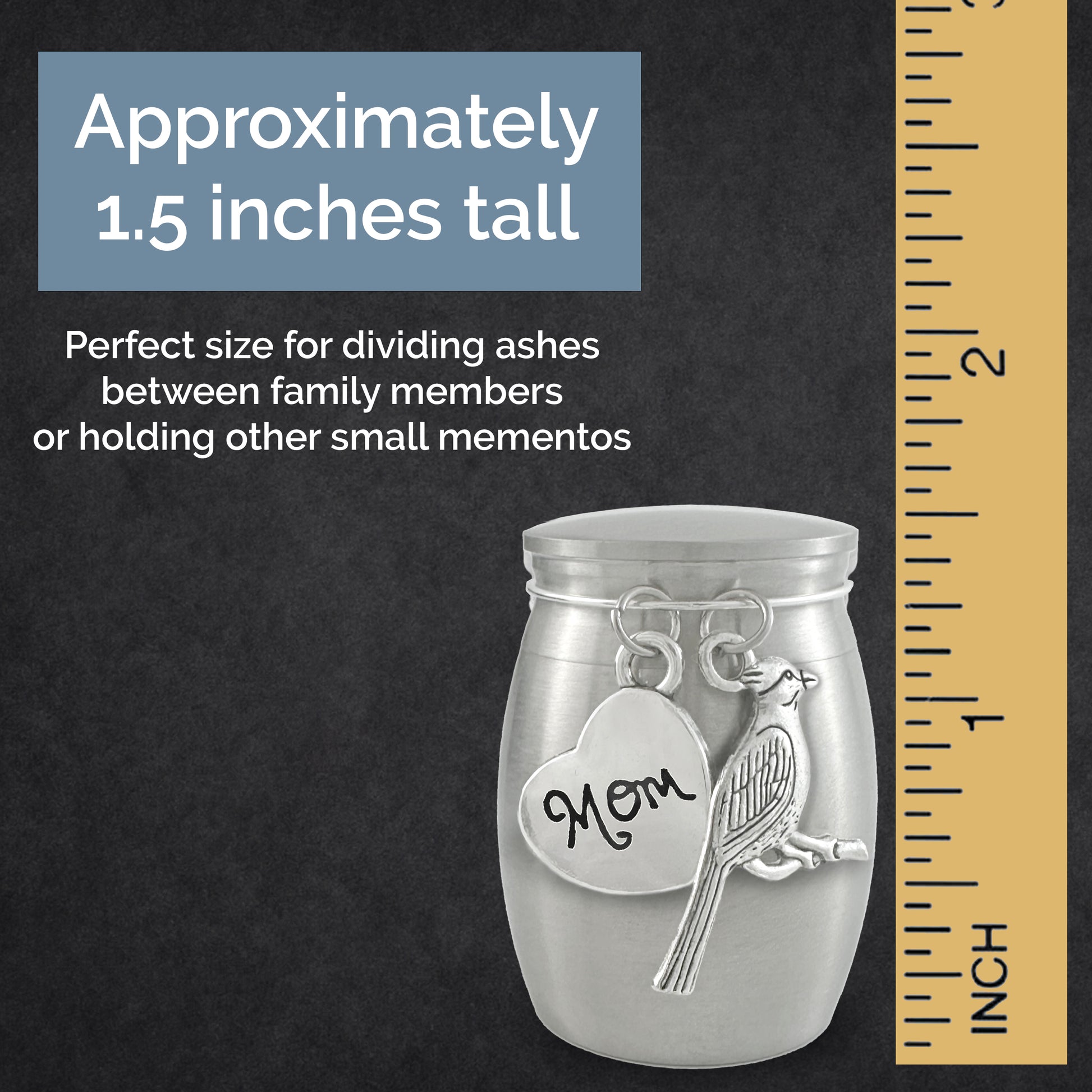 A brushed silver keepsake urn featuring a heart-shaped tag engraved 'Mom' and a cardinal bird charm, shown on a dark textured background with a yellow inch ruler and text stating it is approximately 1.5 inches tall.