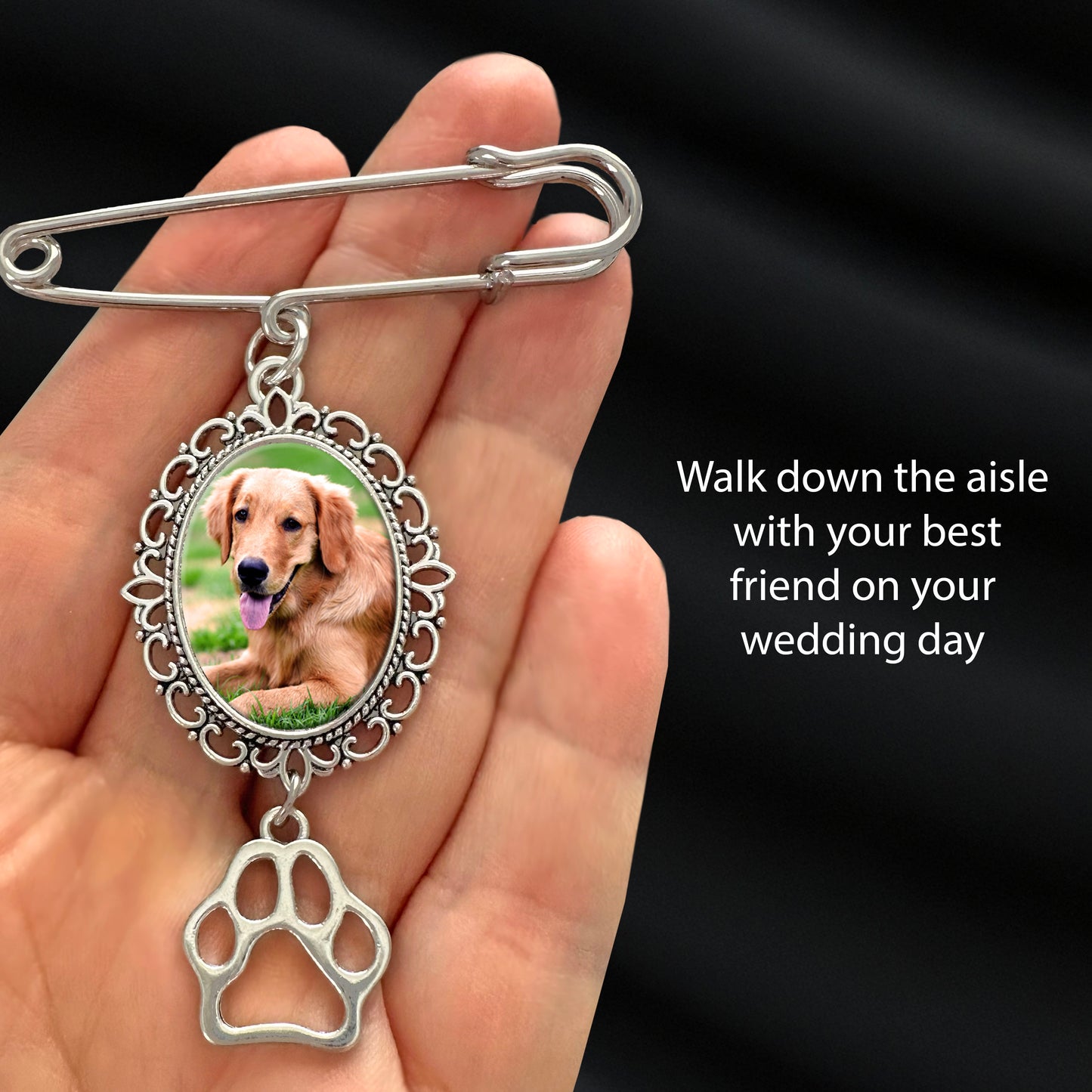 Silver brooch with a photo of a dog and a paw print charm, held in a hand against a black background.