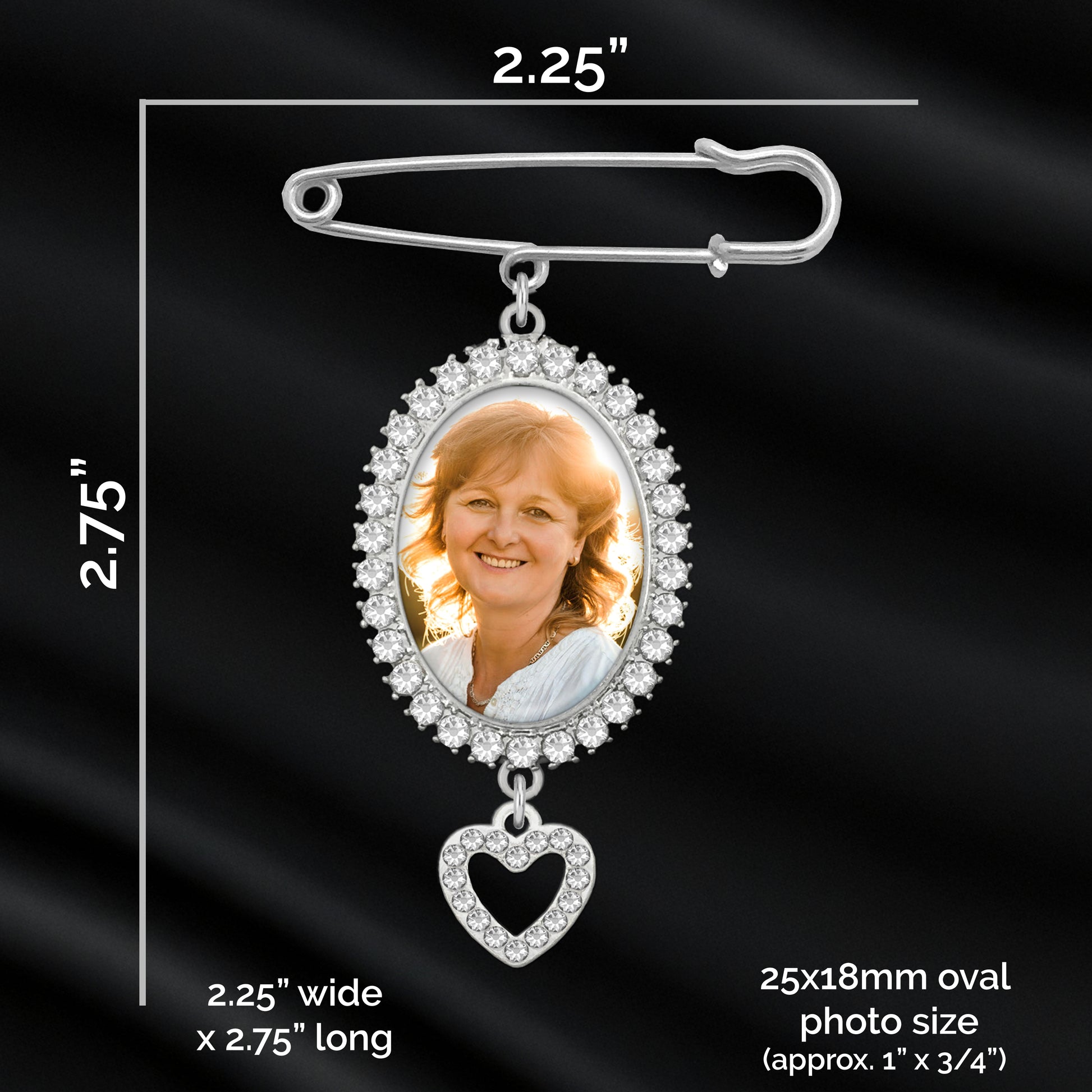 Silver oval photo pendant memorial pin with a heart-shaped dangling charm, shown on a black satin background with printed dimensions and text indicating photo size measurements.