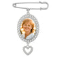 A silver wedding bouquet photo charm pin with an oval photo frame surrounded by clear rhinestones and a dangling heart-shaped rhinestone charm, shown on a plain white background.