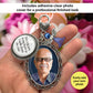 A hand holds a silver-toned memorial pendant keychain with a photo of a man, a round silver charm with text, and decorative blue angel and heart shaped clip. The background is blurred pink flowers, with text overlays reading 'Includes adhesive clear photo cover for a professional finished look' and 'Easily add your own photo'.