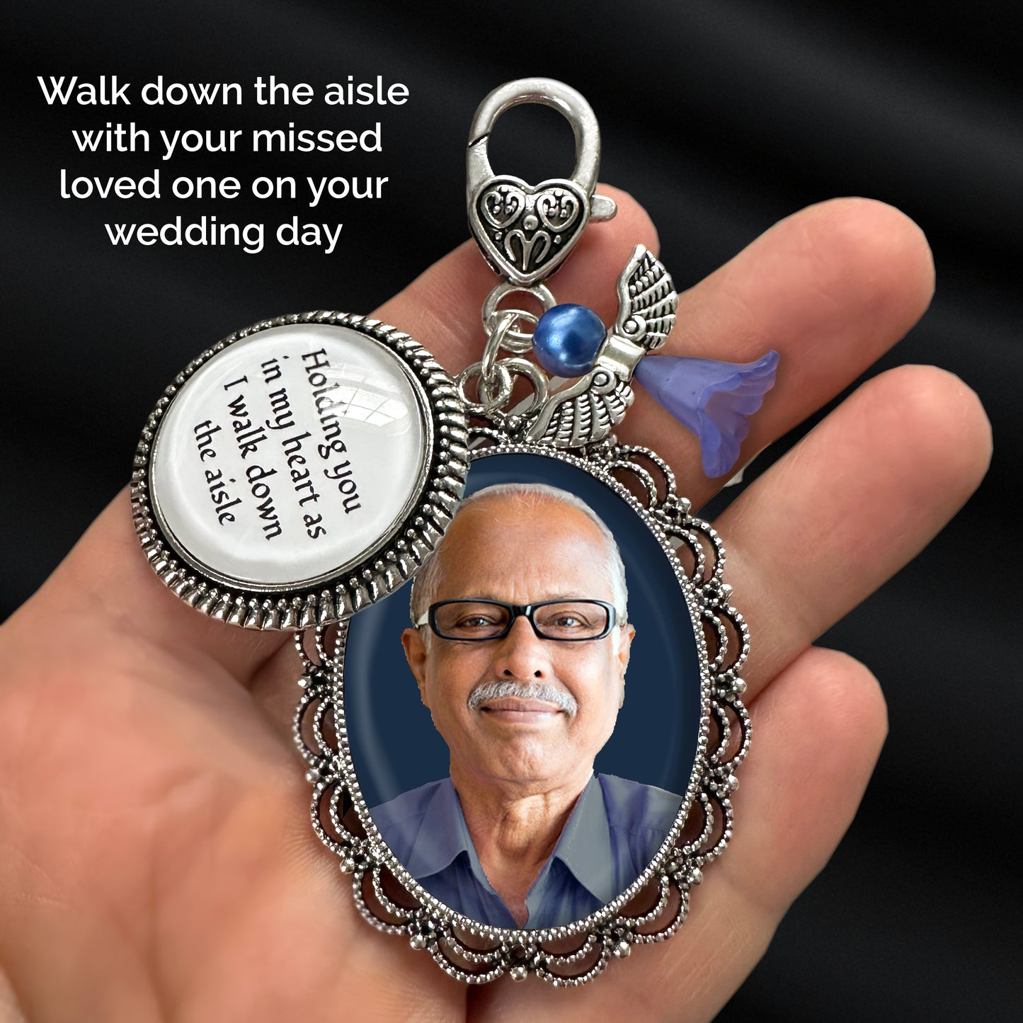 A hand holding a silver-toned keepsake pendant with an oval photo frame, a round photo charm, a something blue angel charm. White text in the upper left reads, 'Walk down the aisle with your missed loved one on your wedding day.