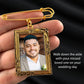 Gold-framed pendant with a photo of a man, held by a hand against a black background.